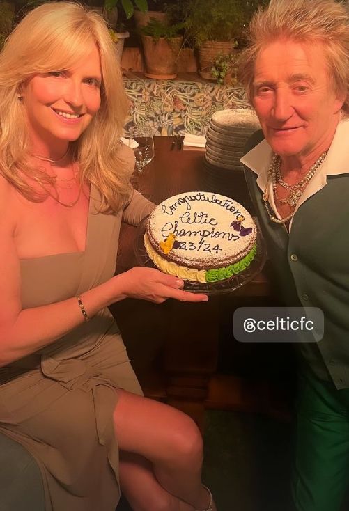 Penny Lancaster in a tan dress holding a cake alongside Rod Stewart in a green outfit