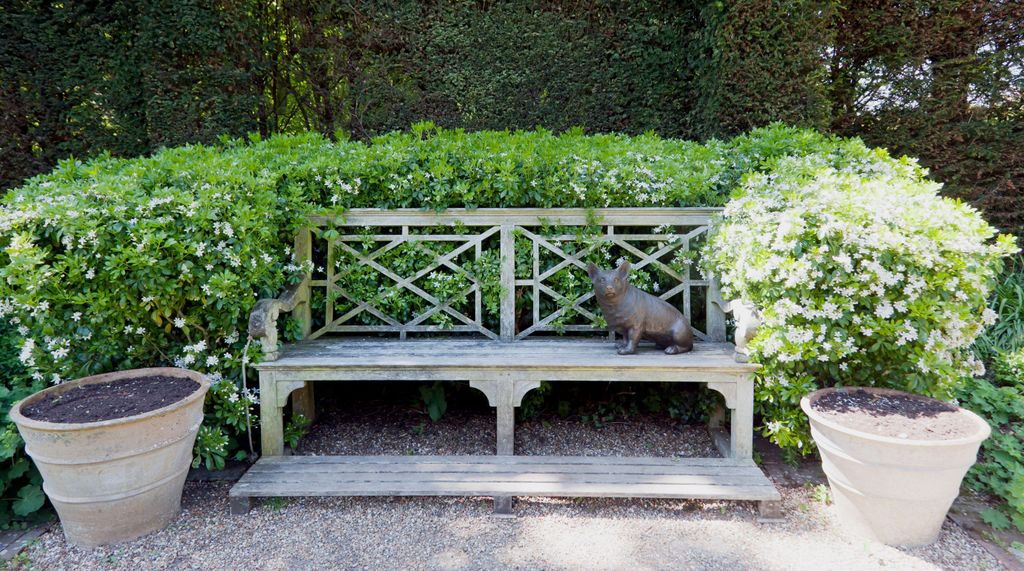 A wooden bench sits in the Queen Mother's Garden featuring a sculpted Corgi