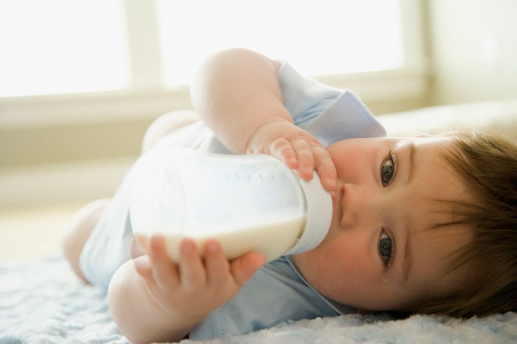 baby drinking milk from bottle led on floor