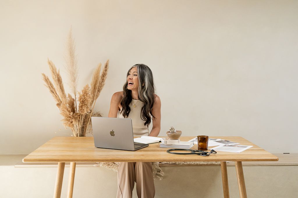 grey haired woman smiling widely working at a wooden desk
