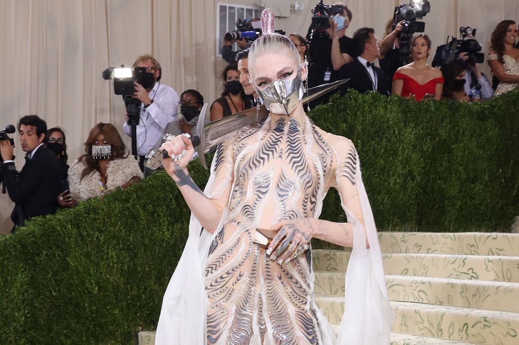 Grimes at the Met Gala 2021 wearing a metal mask and holding a sword on her shoulder