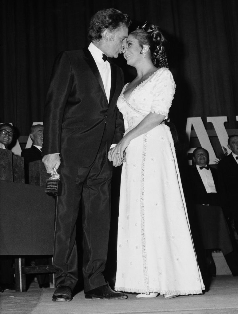 Elizabeth Taylor wearing a white wrap gown and looking up at Richard Burton