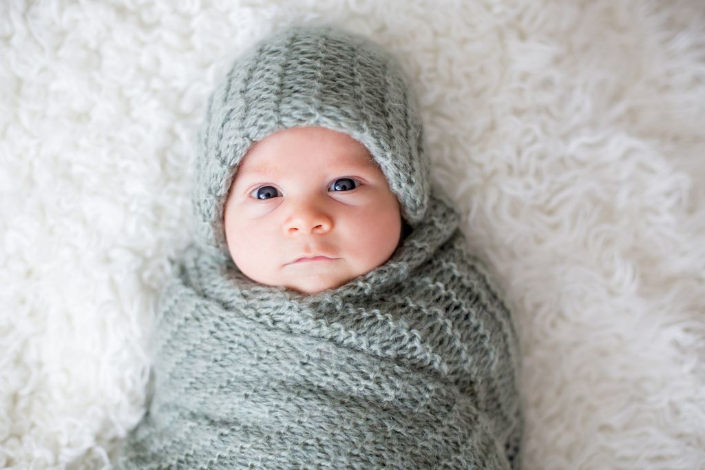 Little newborn baby boy, looking curiously at camera, lay dawn in bed