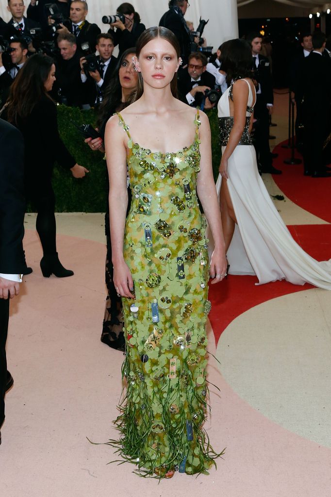 Mia Goth at the 2016 Met Gala wearing a green sequinned slip dress with feathered hem and a ponytail