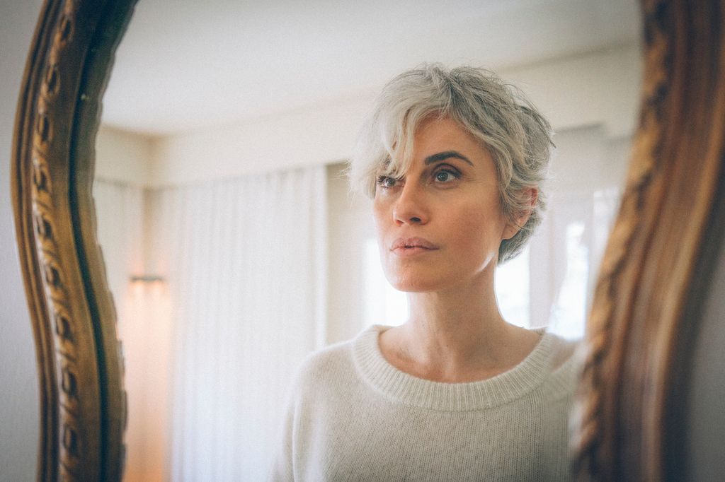 An ageless, short-haired woman examines herseÅf by the mirror