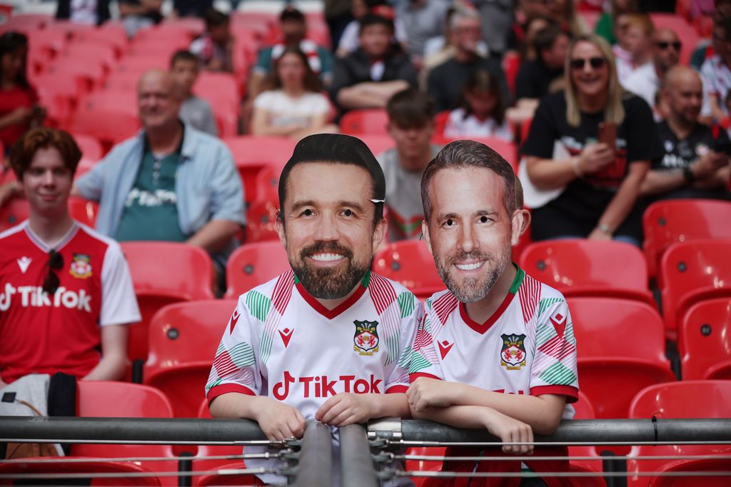Wrexham fans wear new masks featuring Wrexham owners Rob McElhenney (left) and Ryan Reynolds (right), 