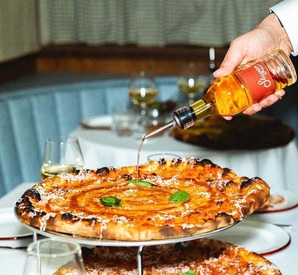 Les meilleures choses à faire à Londres en mars 2026 : une pizza chez Slayer, un avant-goût de la Turquie chez Levent Börek 1 bras de serveur versant de l'huile de piment sur une pizza