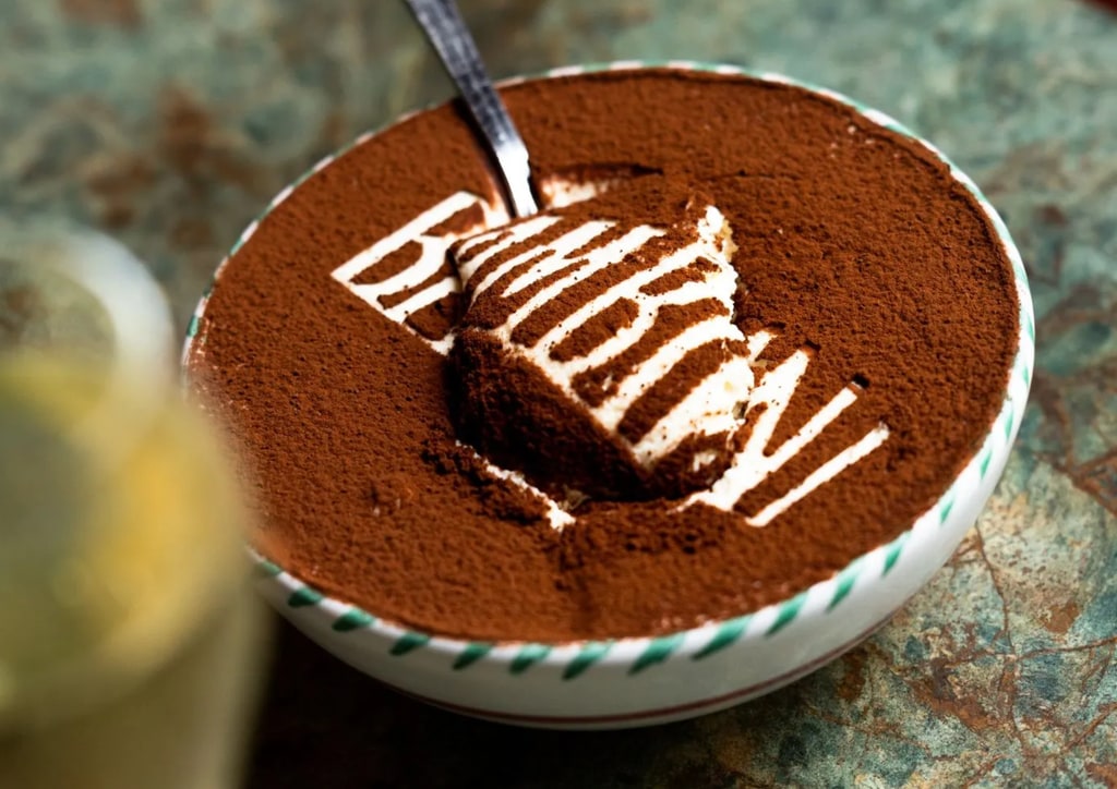 table with a bowl of tiramisu on with a spoon in