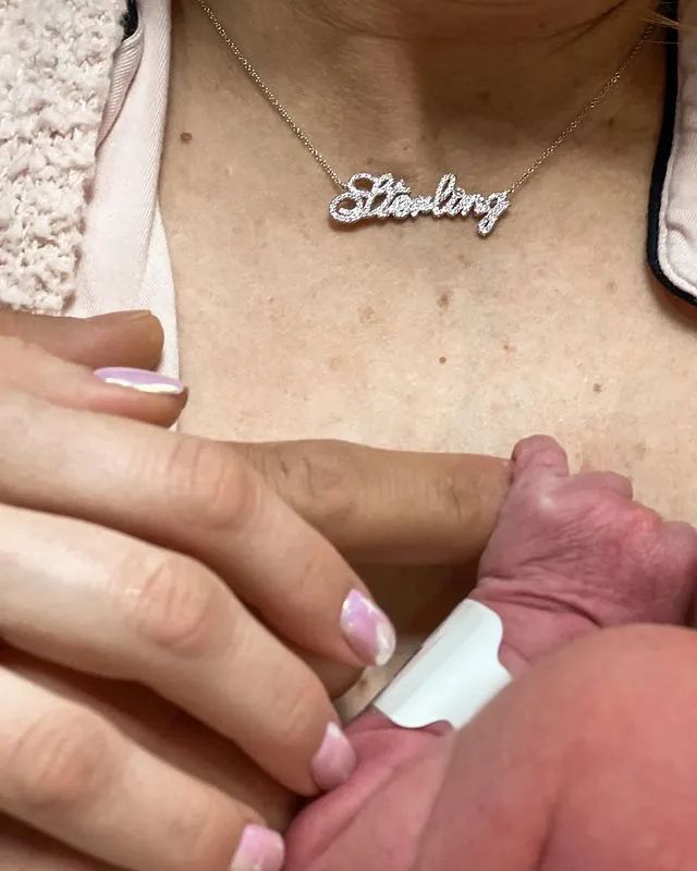 Brittany Mahomes neck is visible with a necklace that reads 'Sterling' as a newborn lies on her chest