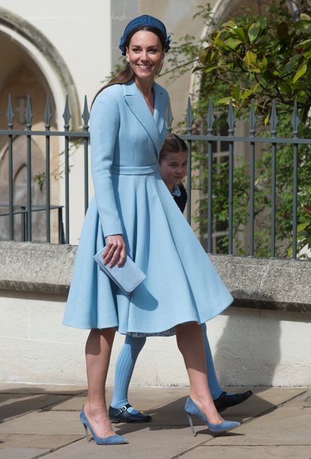 kate wears a full skirted coat dress in a light blue hue with matching suede heeled court shoes and her clutch bag matches the outfit but her choice of navy blue hairband blends with dark brown hair as she walks outside with little charlotte just visible on the far side