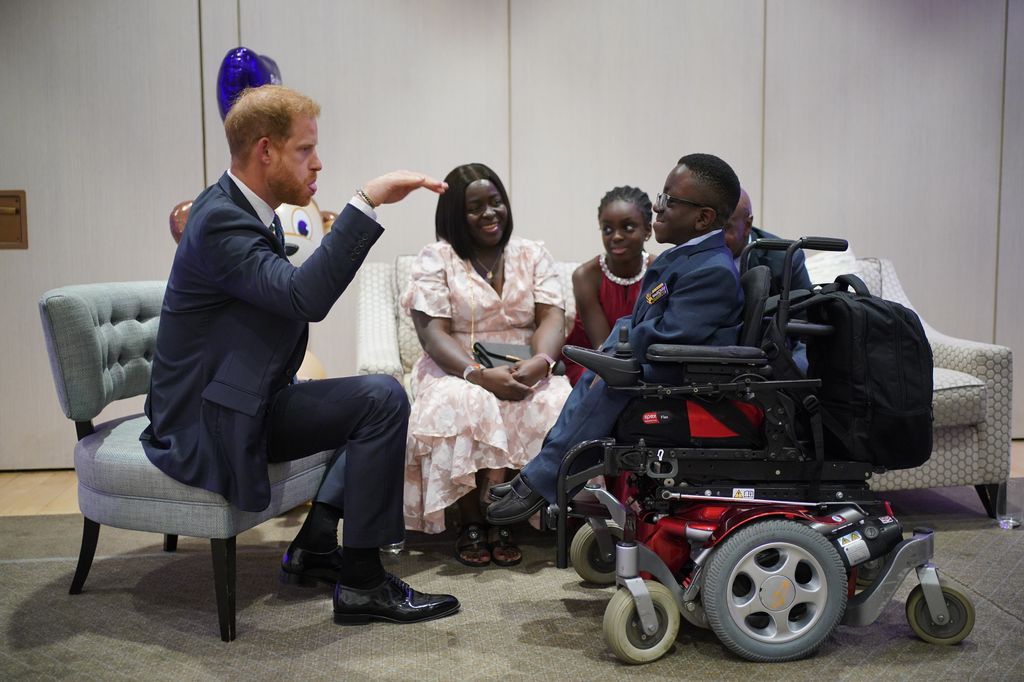 Prince Harry wearing a suit and sitting in a chair whilst making a boy laugh