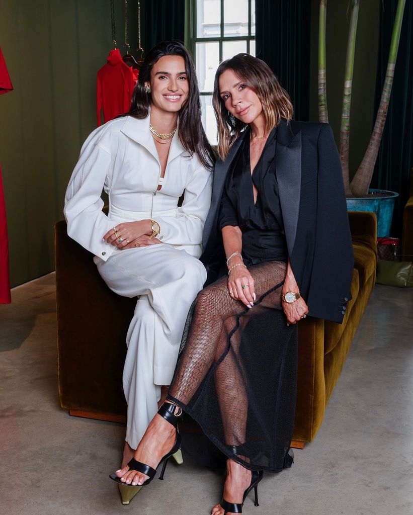 Victoria Beckham est assise sur le bord d'un canapé avec Isabela Grutman qui porte un deux pièces blanches avec des bijoux en or. 