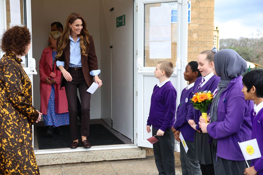 La princesse de Galles en costume marron saluant les enfants en uniforme violet