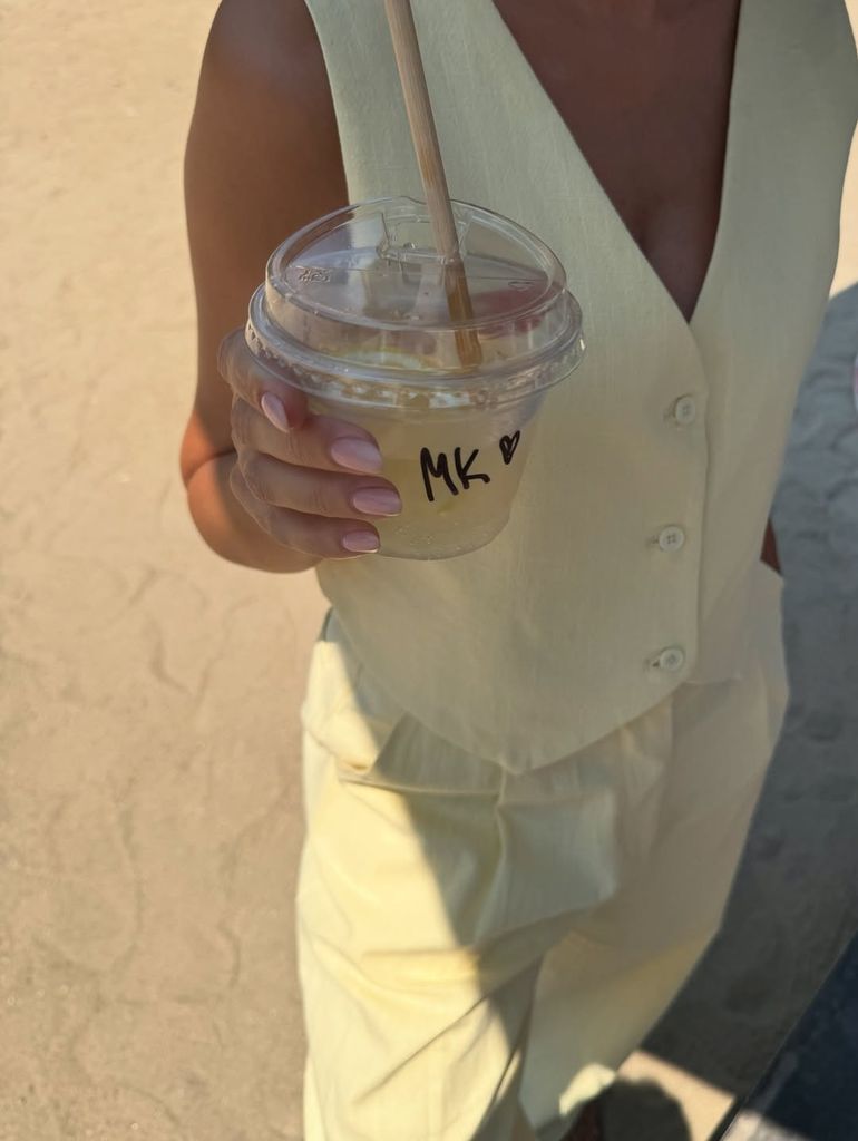 Michelle Keegan wears a butter yellow waistcoat and trouser set and holds an iced coffee