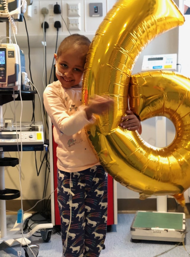 little girl in hospital holding 6 balloon