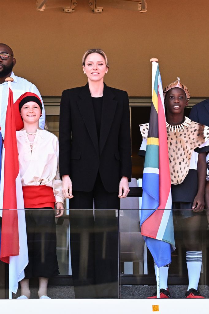 Princess Charlene in a black suit stood up straight beside people