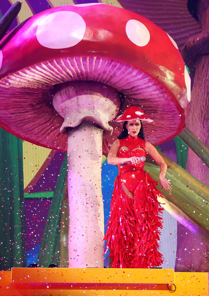 Katy Perry in a red dress and mushroom hat on stage with confetti around her