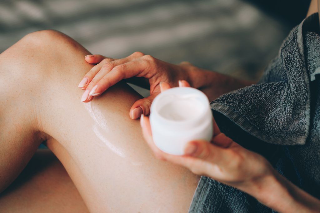 A detailed close-up image of a woman gently applying a moisturizing cream to her legs. The photo captures soft, natural light highlighting the smooth skin texture and delicate manicure, evoking a sense of self-care and wellness. This serene moment is perfect for promoting skincare products, beauty routines, or wellness-related content.