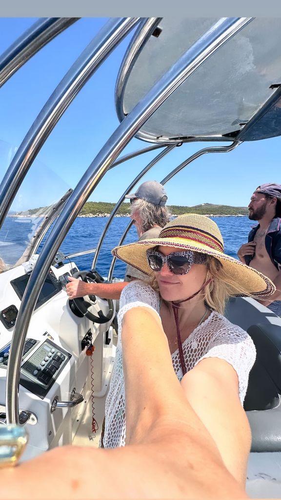 Kate Hudson com uma blusa de malha branca e chapéu em um barco