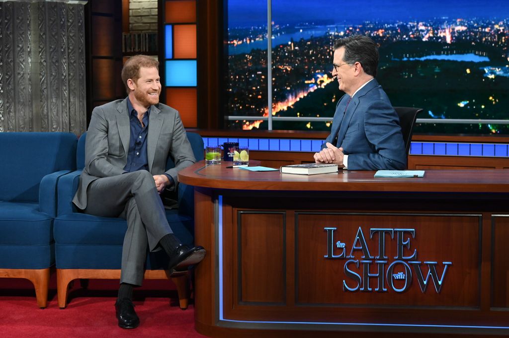 Prince Harry and Stephen Colbert both smiling at each other, dressed in suits and sat relxed in chairs