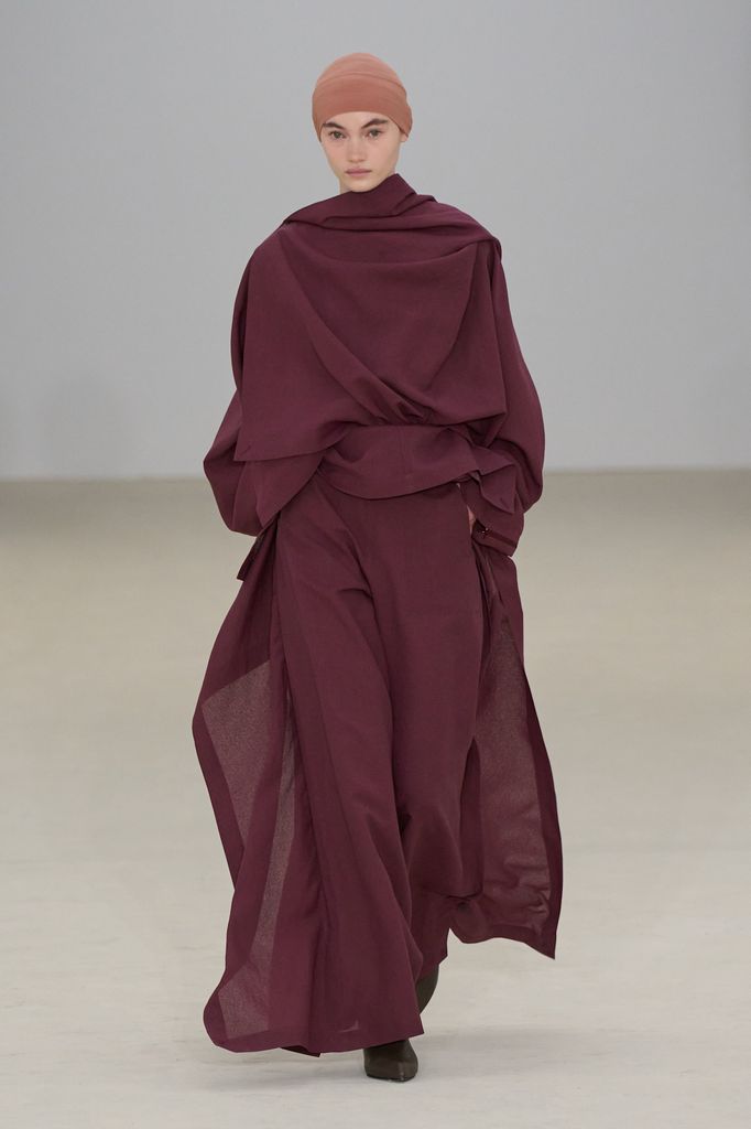 A model walks down the runway swathed in oxblood coloured floaty cape top and matching trousers