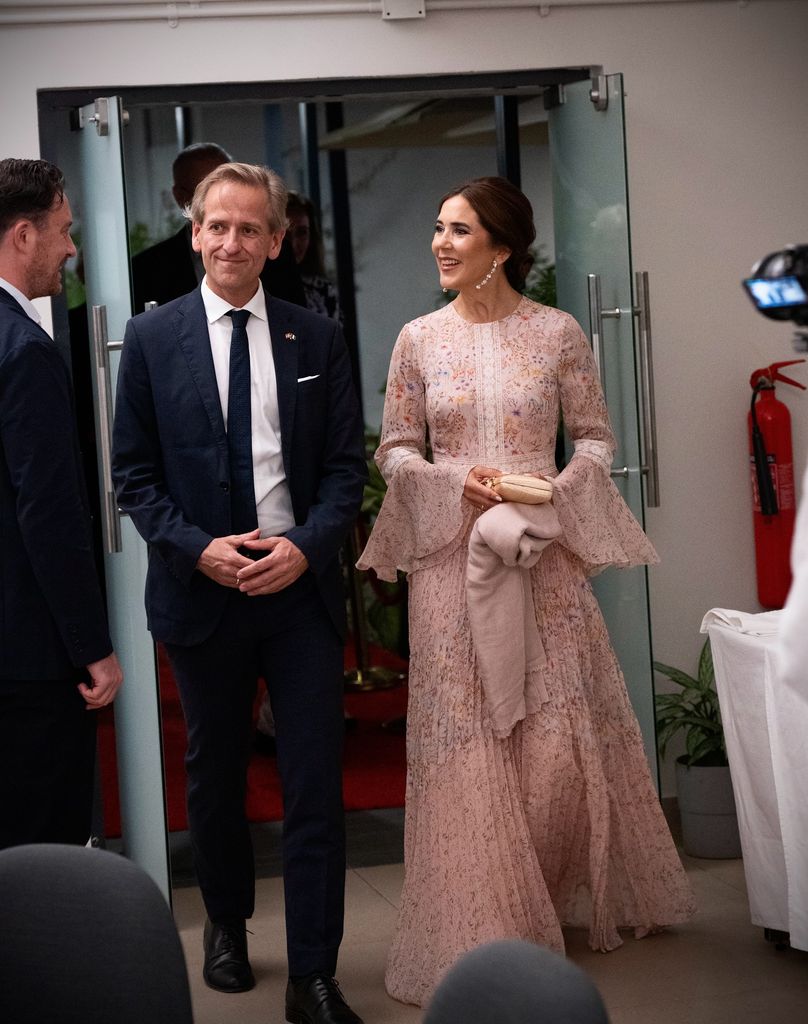 queen mary in pink dress walking into room with man