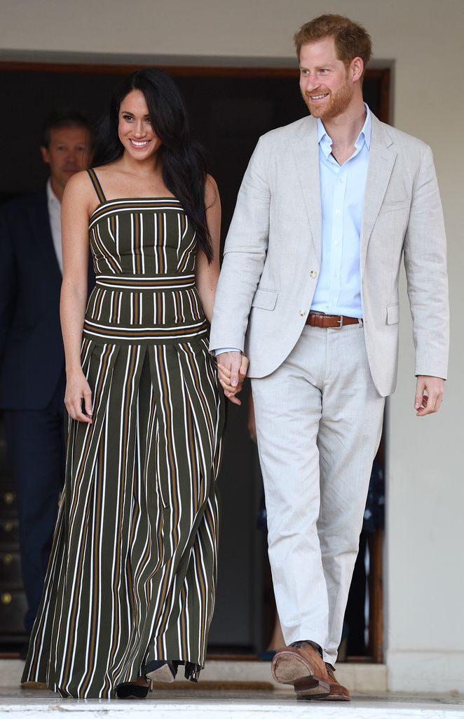 Prince Harry, Duke of Sussex and Meghan, Duchess of Sussex in blacks stripy dress walking hand in hand