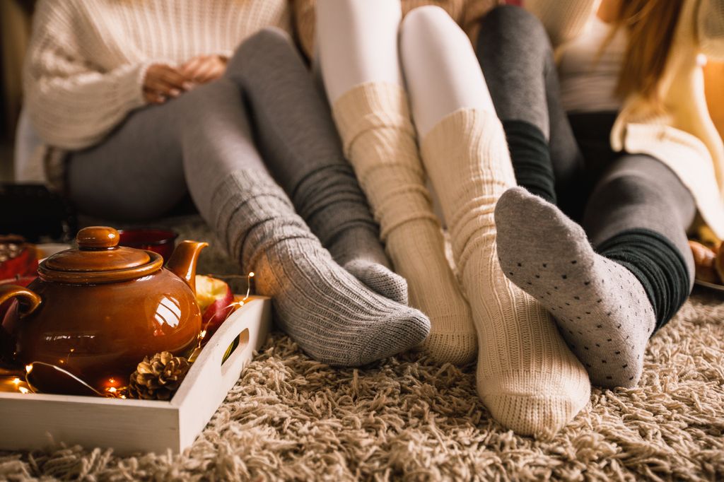 Lower section of three unrecognizable young girlfriends sitting on the bedroom floor in their cozy socks and hanging out together while enjoying some warm tea on a cold autumn day.