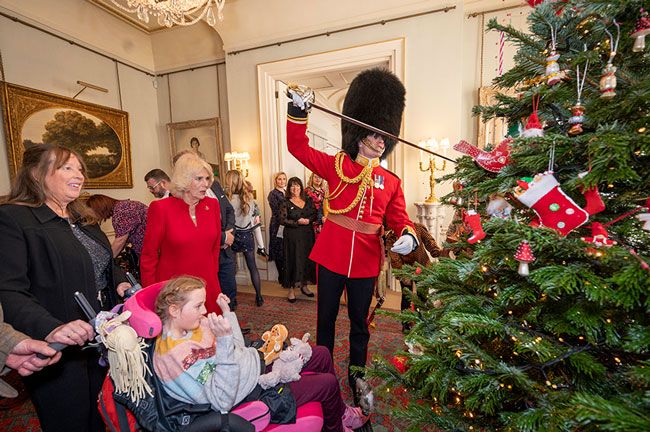 The Queen Consorts equerry places decorations on the Christmas tree with a sword