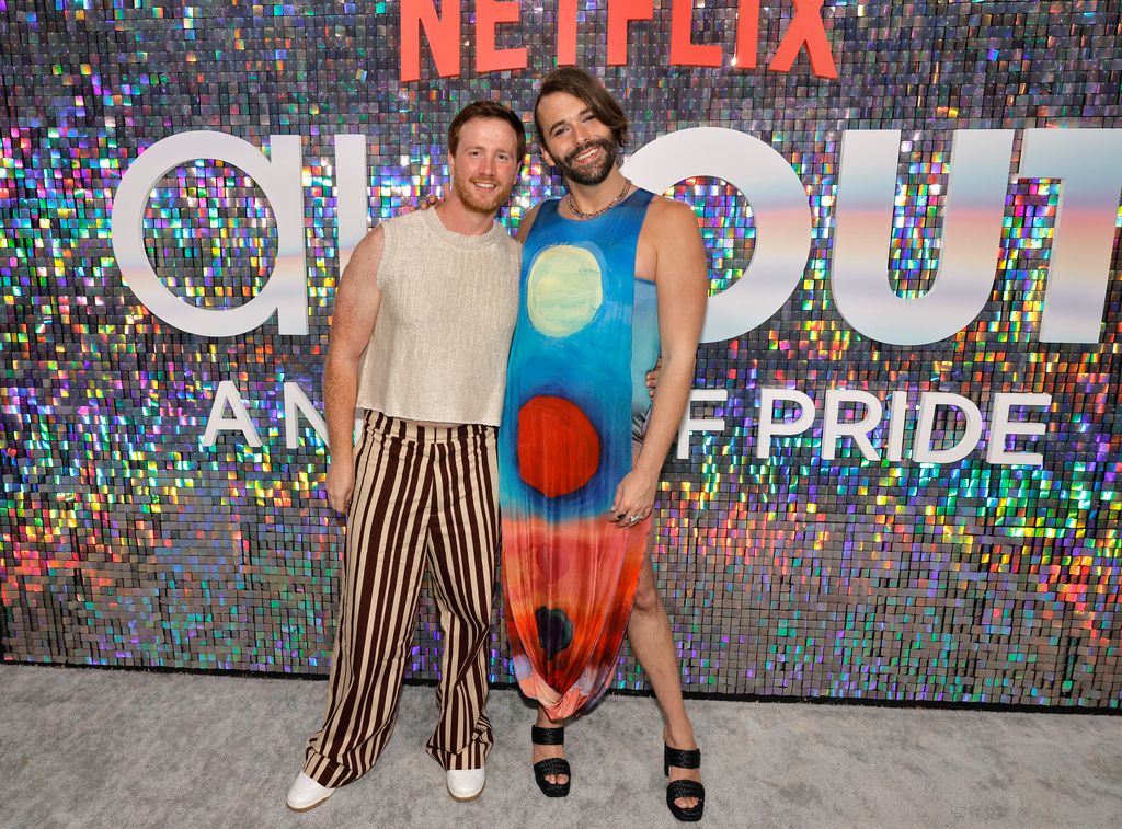 Mark Peacock in a biege top and stripy trousers with arms around Jonathan Van Ness in a colourful floaty dress