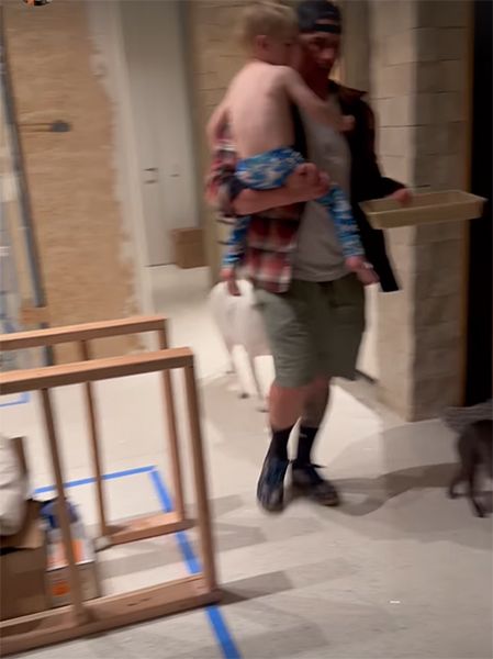 Josh Hall walking through unfinished kitchen carrying burgers and a child