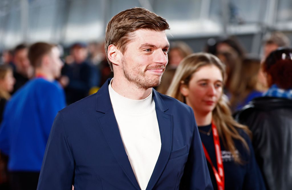 Max Verstappen smiling in a blue blazer and white high neck top