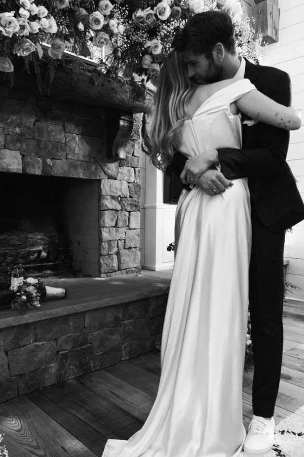 Miley Cyrus in her wedding dress hugging Liam Hemsworth in a suit