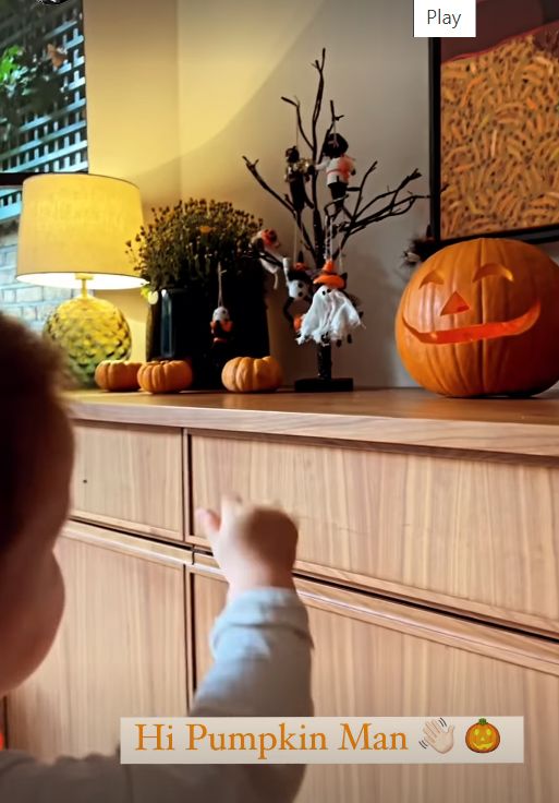 A young child waving at a pumpkin