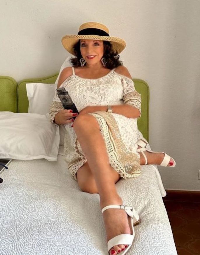 Joan Collins sat on a bed wearing a lacy white dress