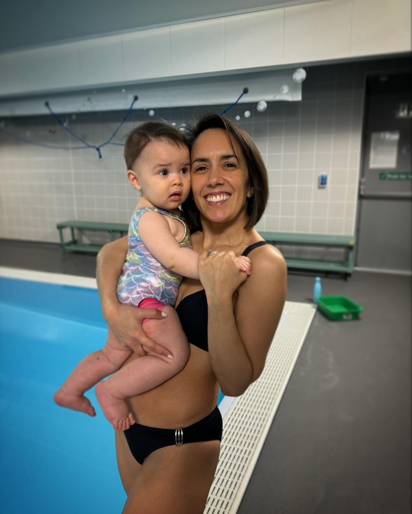 mother in bikini holding daughter by swimming pool