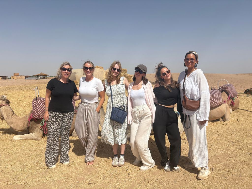 A group of six girls posing in front of camels in the desert