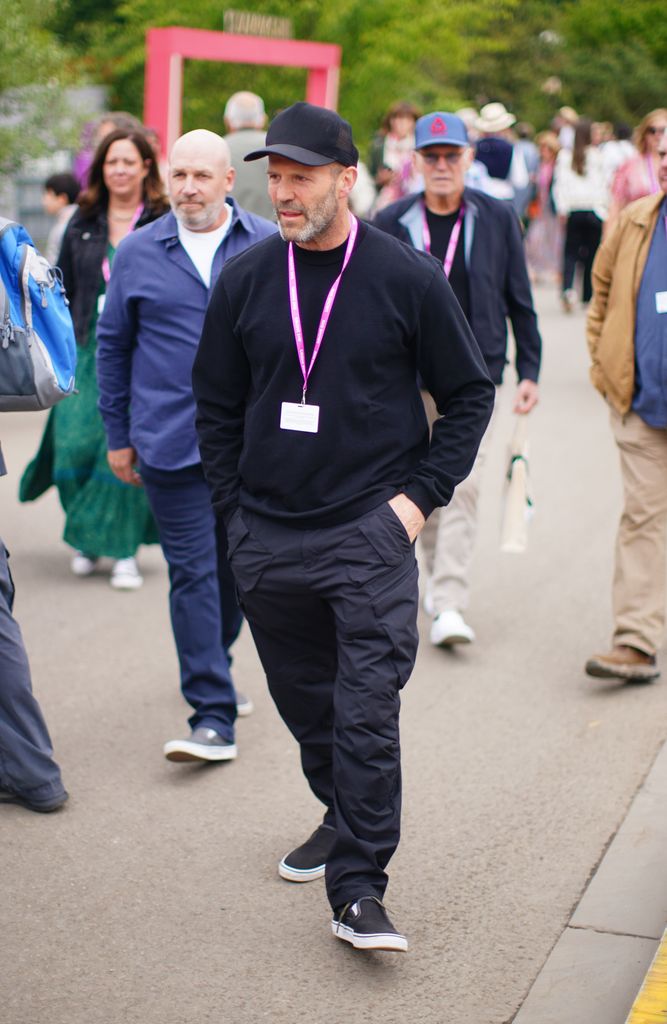 Jason Statham walks through Chelsea Flower Show in an all-black outfit with a cap, sweatshirt and cargo trousers, blending cool and casual.