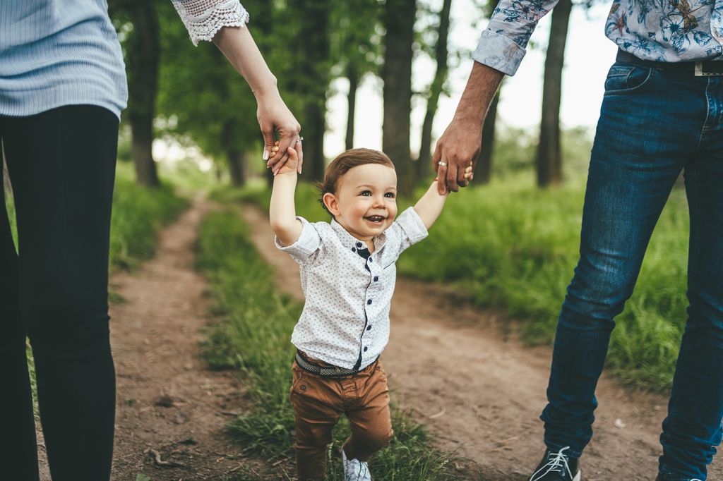 Mother and father outdoors teaching baby boy to walk