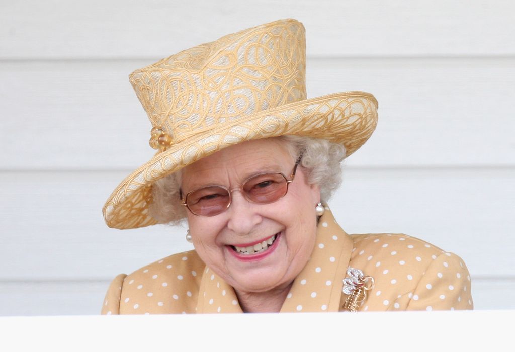 SM la reine Elizabeth II riant avec un chapeau et une robe jaune pâle