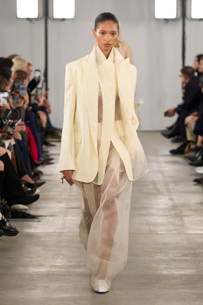 A model wears a cream blazer with sheer mesh cream trousers