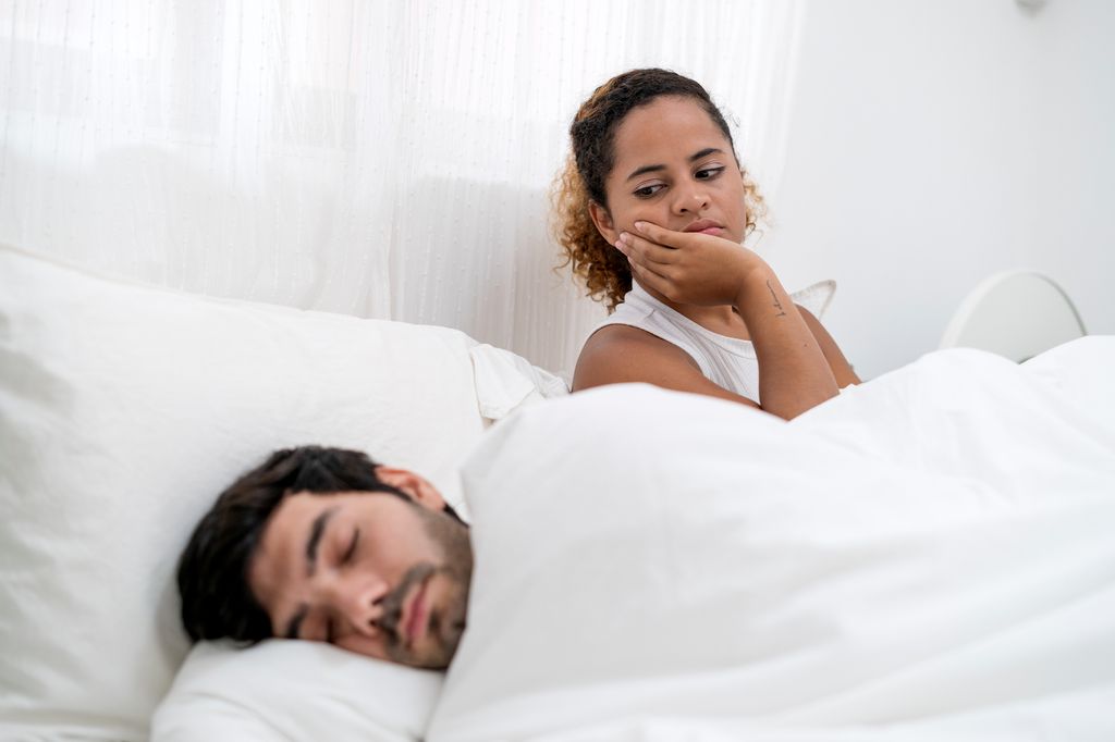 Frustrated girlfriend sad in bed thinking of relationship problems while boyfriend sleeping beside her.