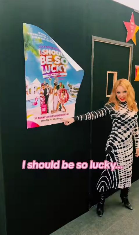 Kylie Minogue in black and white dress next to a poster falling down