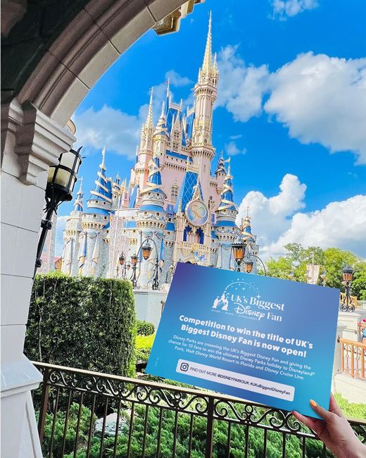 a disney competition card held out in front of a real disney castle 