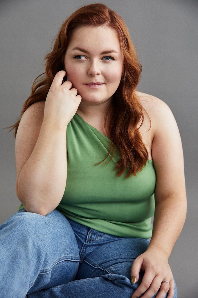 Lucy Edwards has wavy hair and is wearing a green top and jeans while posing for the camera