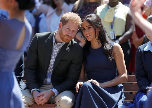 Prince Harry and Meghan Markle sitting outside smiling and whispering to each other