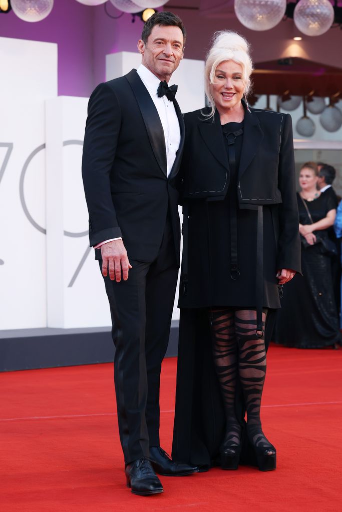 Hugh Jackman in a black suit and his wife in striped tights