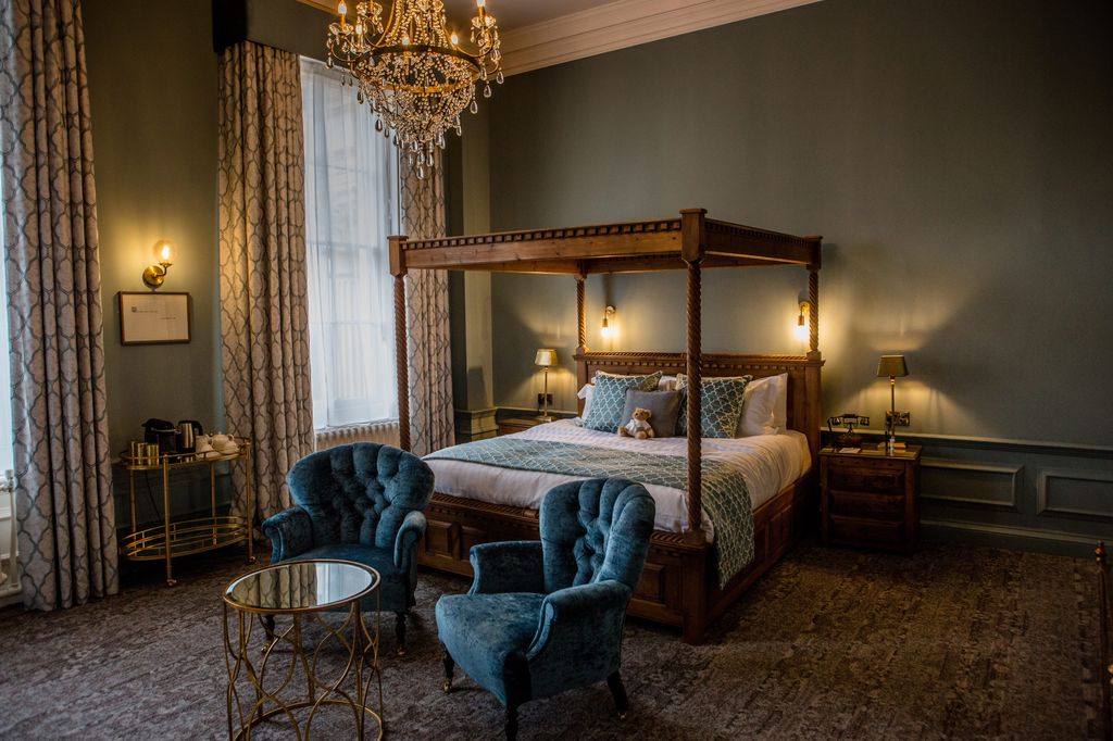 A bedroom with four-poster bed and two blue armchairs