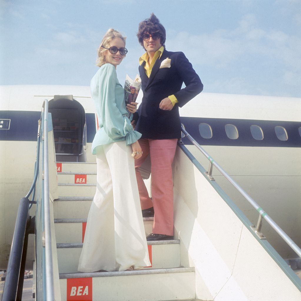 Arriving at the airport with flair, Twiggy and her partner make a bold entrance. She sports wide-leg pants, pastel hues, and oversized sunglasses, a classic look for jet-setting fashionistas of the time. This polished yet relaxed style signals the shift towards more glamorous, travel-friendly fashion.