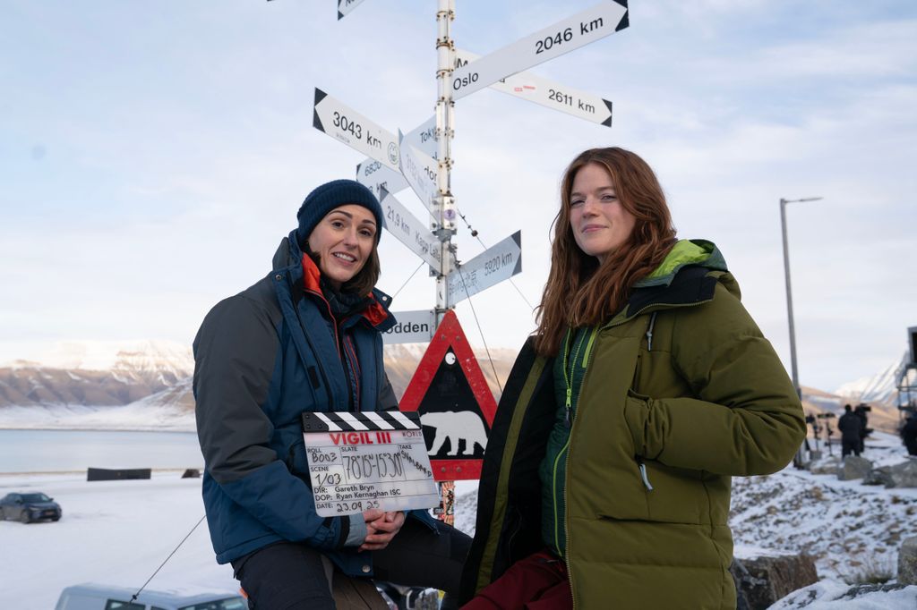 Two women stand with a clapperboard in snow